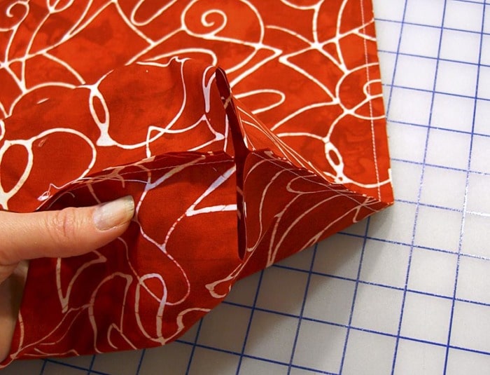 Close-up showing how to bring side seam and bottom seam together to box the bottom corner of a fabric bag.