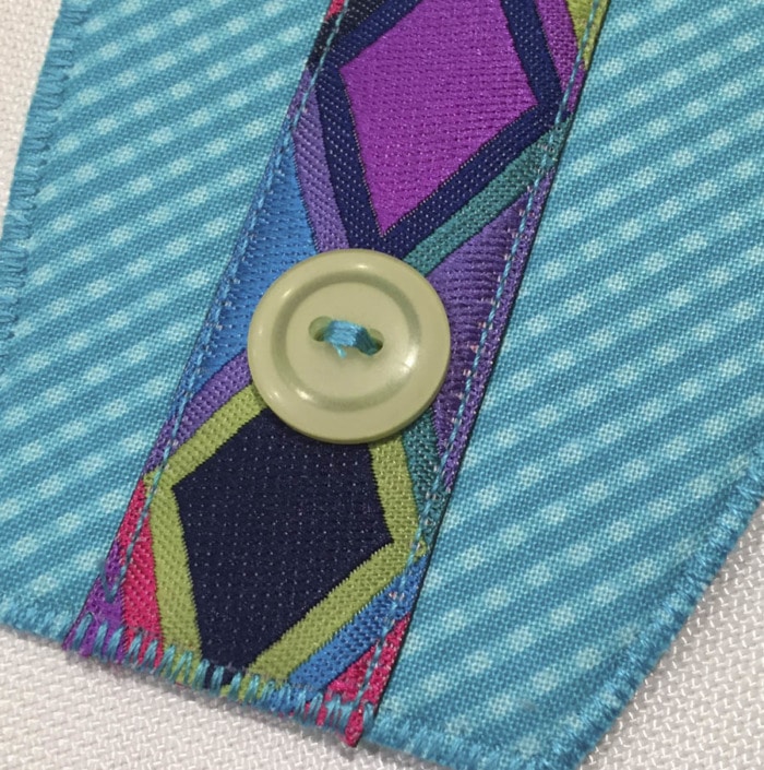 Close up picture of a button sewn in place on top of decorative ribbon on a Button Boats organizer.