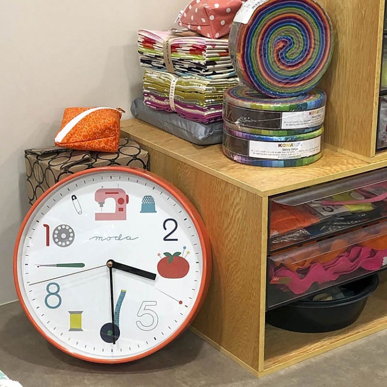 Close-up of an orange colored sewing themed wall clock. A clock like this is a perfect sewing gift for stitchy friends